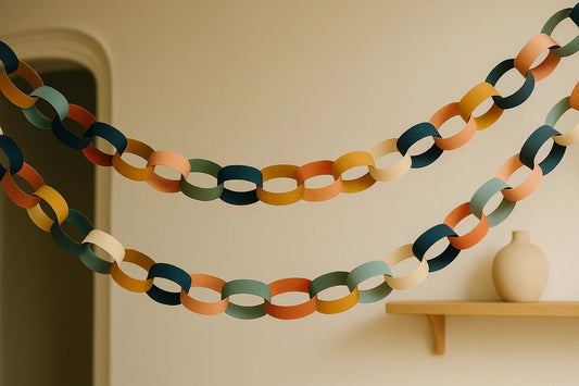 Colorful handmade paper garlands hanging across a softly lit room with an archway and a small wooden shelf.