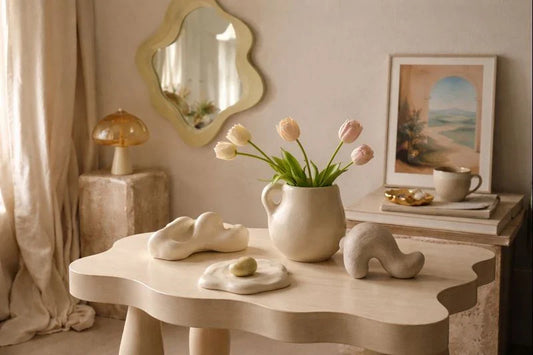 Soft surreal interior with sculptural wooden table, abstract ceramic objects, tulips in a handmade vase, and warm natural light