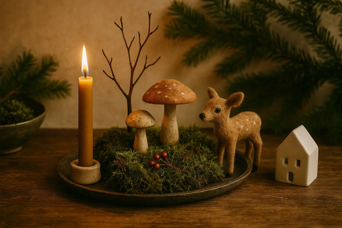 A mossy woodland Christmas vignette with a candle, tiny mushrooms, a small deer figure, and evergreen branches on a wooden table.