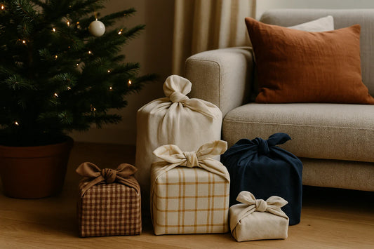 Fabric-wrapped Christmas gifts arranged beside a lit tree and a sofa in a warm, cozy living room.