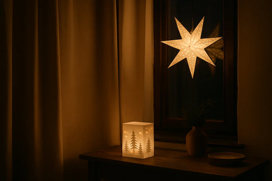 Warm-lit window scene with paper star lantern and cut-paper luminary on table, casting soft shadows in a cozy room.