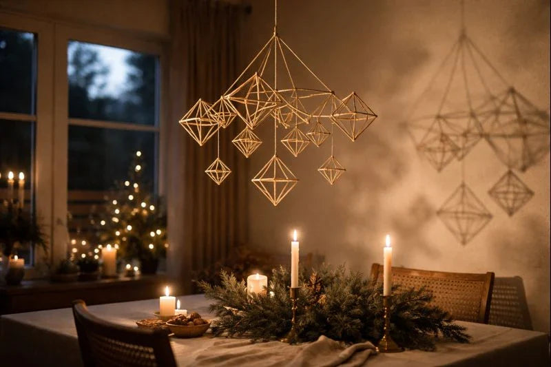 Straw himmeli mobile hanging above a candlelit dining table with evergreen greenery and soft Christmas lights in a cozy winter interior.
